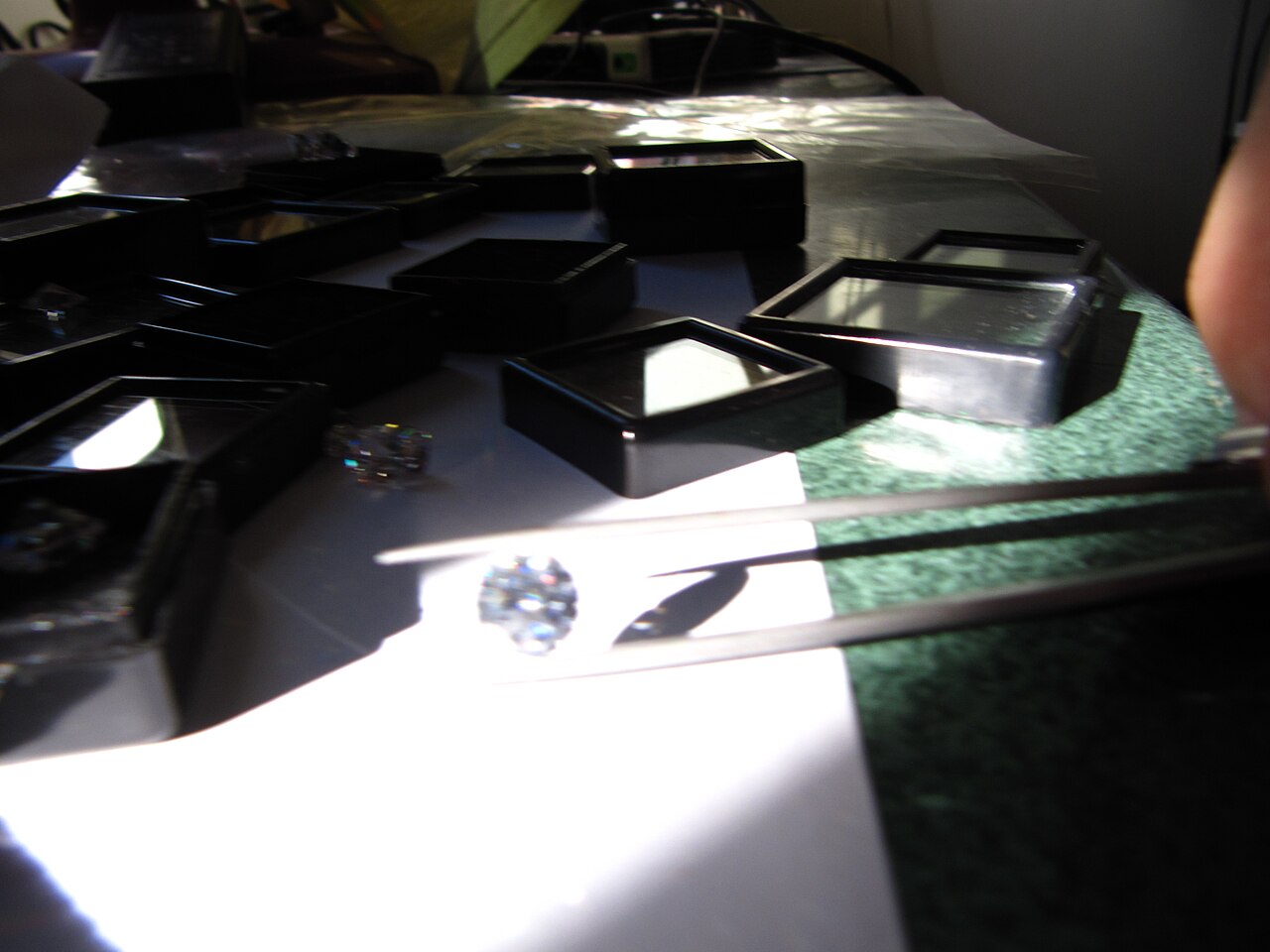 A diamond held in tweezers in bright sunlight on a jeweller’s bench