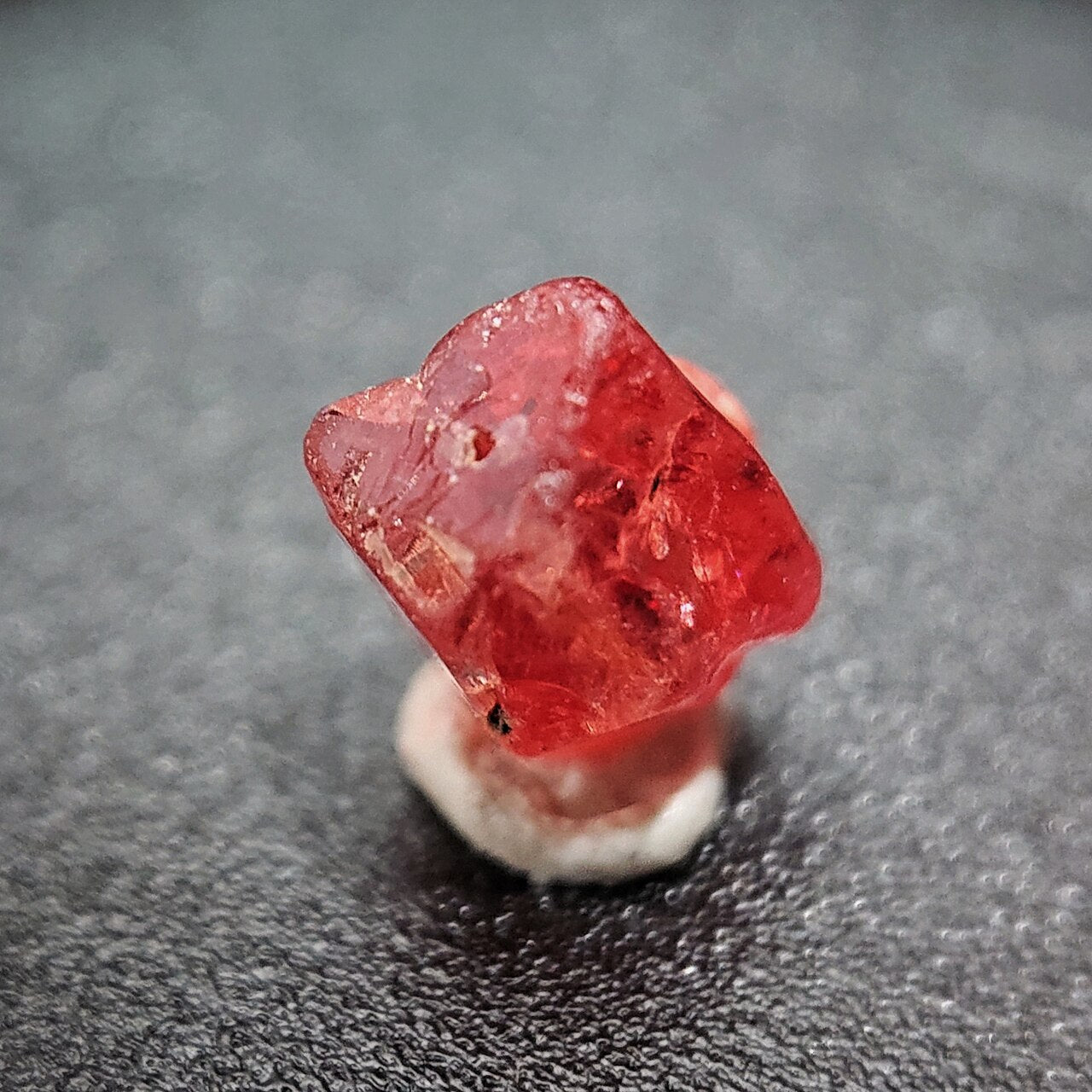 An uncut red spinel crystal on a grey surface