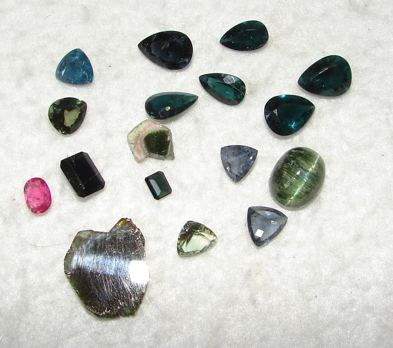 An assortment of green, blue and pink cut tourmalines with a rough crystal